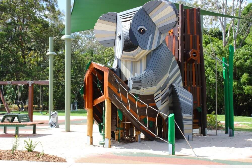 A Koala Playgorund that is made out of wood and has a slide, climbing ropes and a tree.